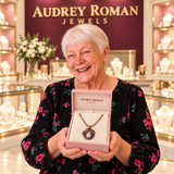A white-haired woman presents the Clara Necklace in an Audrey Roman Jewels box inside the rose and ivory boutique.