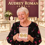 Woman presenting Cassandra flower earrings in an Audrey Roman Jewels box inside an ivory, rose and wine-colored boutique.